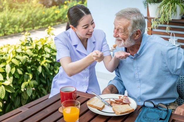 Nurse feeding elderly senior man breakfast